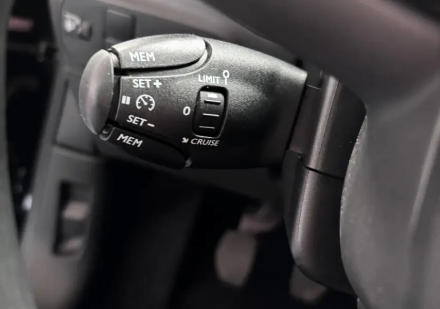 Gros plan sur la commande de régulateur de vitesse à gauche du volant dans l'habitacle noir de la Citroën C3 2024.