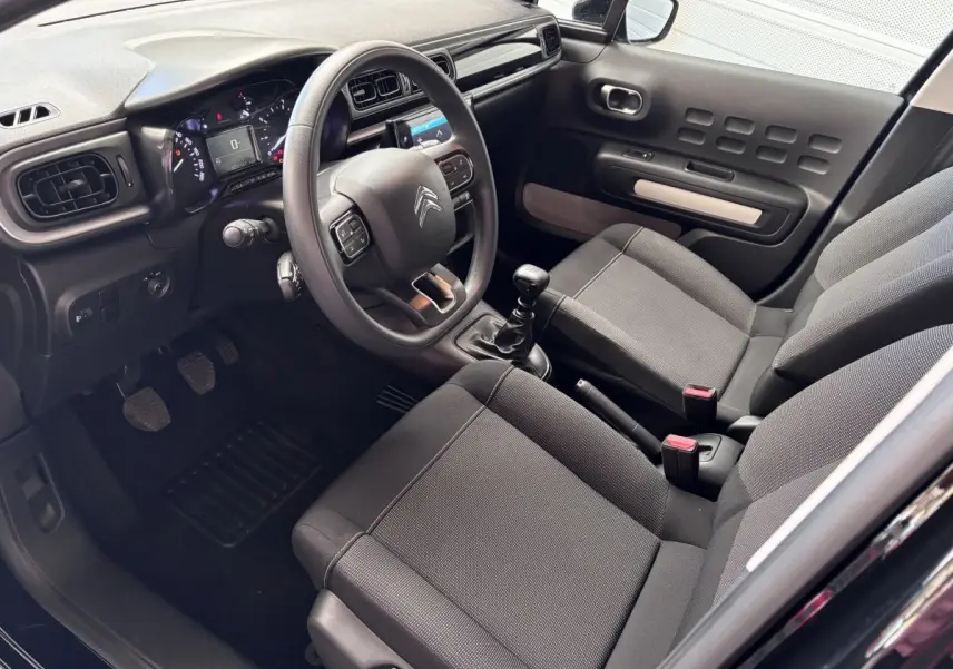 Intérieur avant de la Citroën C3 PureTech 110 noir, vue côté conducteur montrant volant multifonctions et sièges tissu gris.