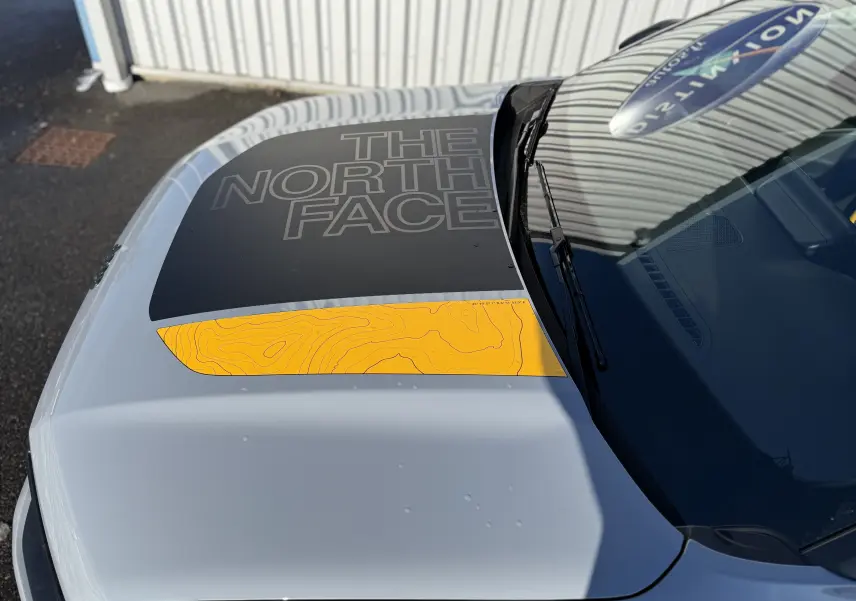 Vue plongeante sur le capot gris Storm Grey du Jeep Avenger 2025 avec sticker noir et jaune "THE NORTH FACE".