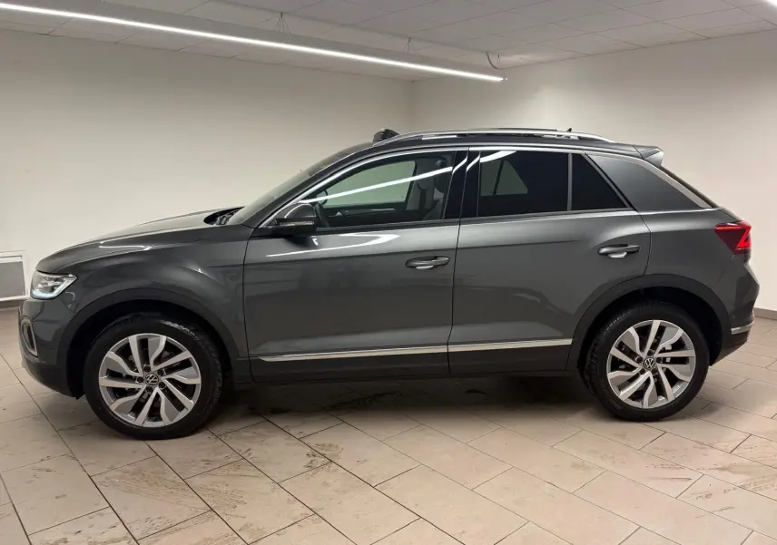 Vue de profil côté gauche d'un Volkswagen T-Roc 2025 gris Indium avec attelage amovible en intérieur.
