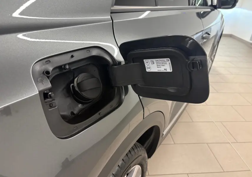 Vue rapprochée de la trappe à carburant ouverte côté gauche d’un Volkswagen T-Roc gris Indium 2025.