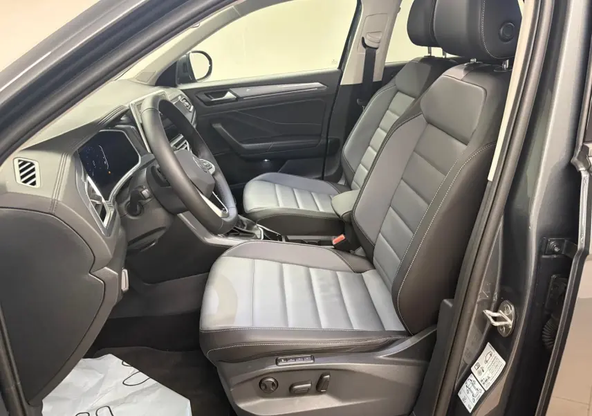 Vue intérieure côté conducteur du Volkswagen T-Roc 2025 avec sièges bi-ton gris et noir, volant multifonctions et tableau de bord moderne.