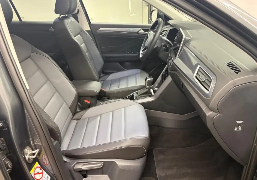 Intérieur avant du Volkswagen T-Roc 2025 en gris Indium, vue côté conducteur avec sièges en cuir et tableau de bord moderne.