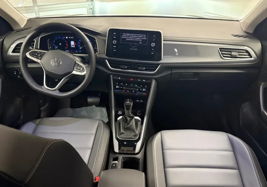 Vue intérieure avant du Volkswagen T-Roc 2025, tableau de bord moderne avec écran central et sièges gris clair.