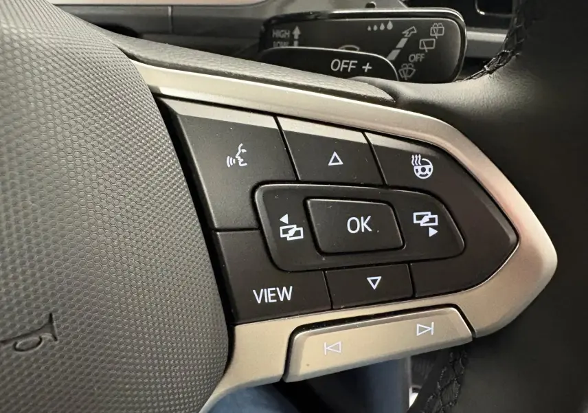 Gros plan sur les commandes au volant du Volkswagen T-Roc 2025, avec finition gris Indium et boutons multifonctions visibles.
