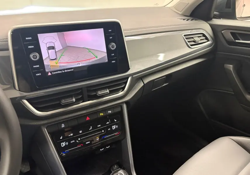Vue intérieure côté passager du tableau de bord du Volkswagen T-Roc 2025, avec écran tactile et commandes climatisation visibles.