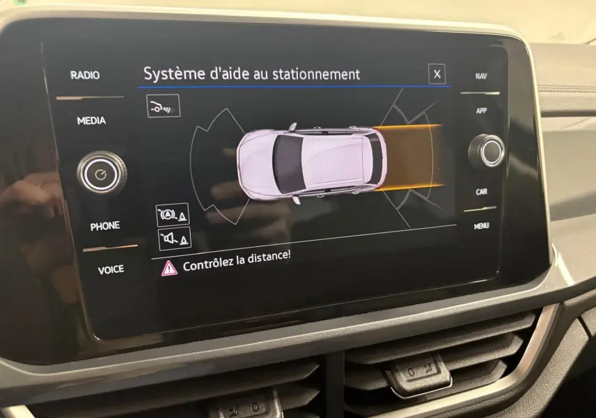 Écran tactile du système d'aide au stationnement du Volkswagen T-Roc 2025 montrant une vue aérienne du véhicule gris Indium.