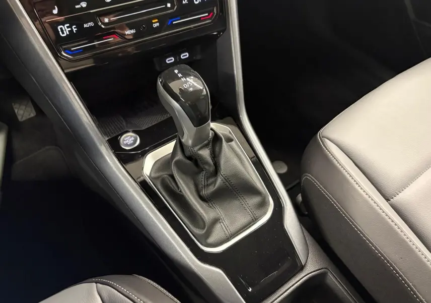 Gros plan sur la console centrale du Volkswagen T-Roc 2025 avec levier de boîte auto et sièges cuir gris.