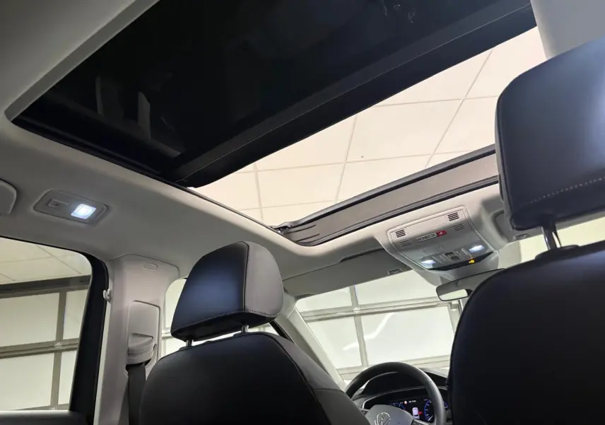Vue intérieure du Volkswagen T-Roc 2025 montrant le toit ouvrant panoramique et les appuie-têtes avant en cuir noir.