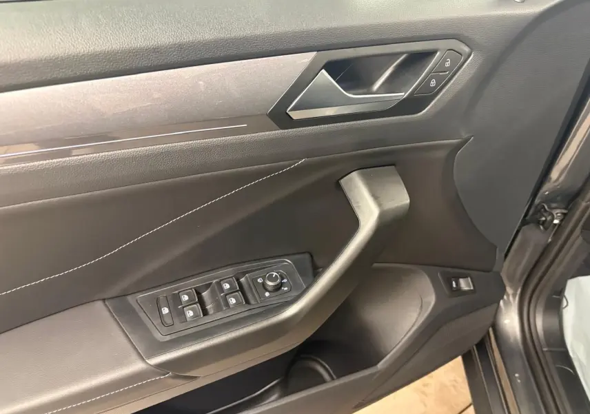 Gros plan sur la porte avant gauche du Volkswagen T-Roc gris Indium, montrant les commandes des vitres et la poignée intérieure.