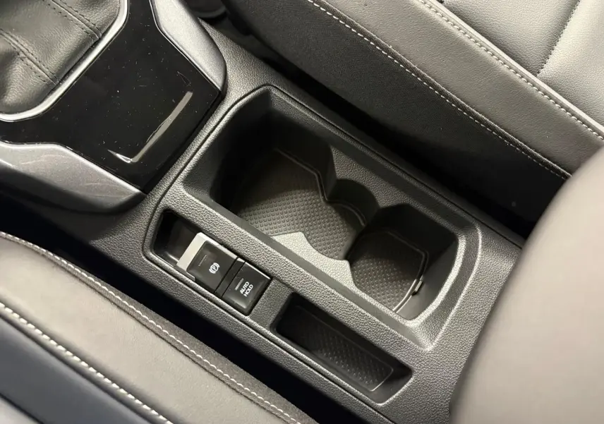 Gros plan sur la console centrale noire du Volkswagen T-Roc 2025 avec porte-gobelets et frein à main électronique.