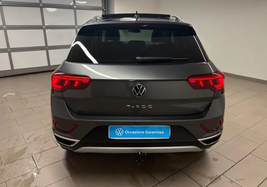 Vue arrière d'un Volkswagen T-Roc gris Indium 2025 avec feux allumés et attelage amovible visible.
