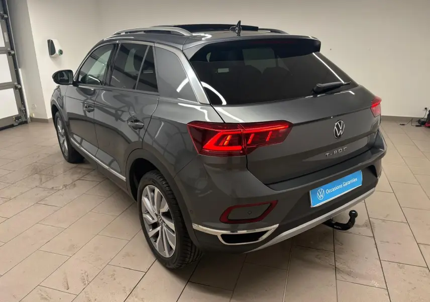 Volkswagen T-Roc 2025 gris Indium vu en 3/4 arrière droit avec attelage amovible dans un garage.