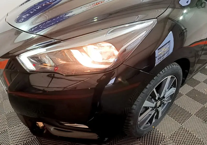 Gros plan sur l'avant droit noir de la Nissan Micra IG-T 90 N-Connecta avec phare allumé et jante alliage visible.