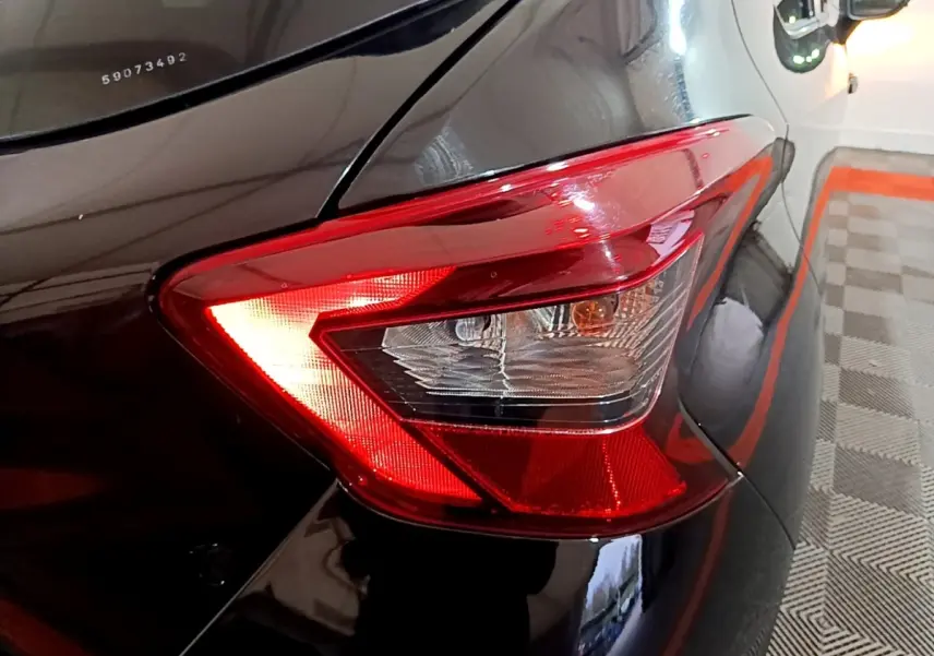 Gros plan sur le feu arrière droit rouge d’une Nissan Micra IG-T 90 N-Connecta noire, avec reflet sur la carrosserie brillante.