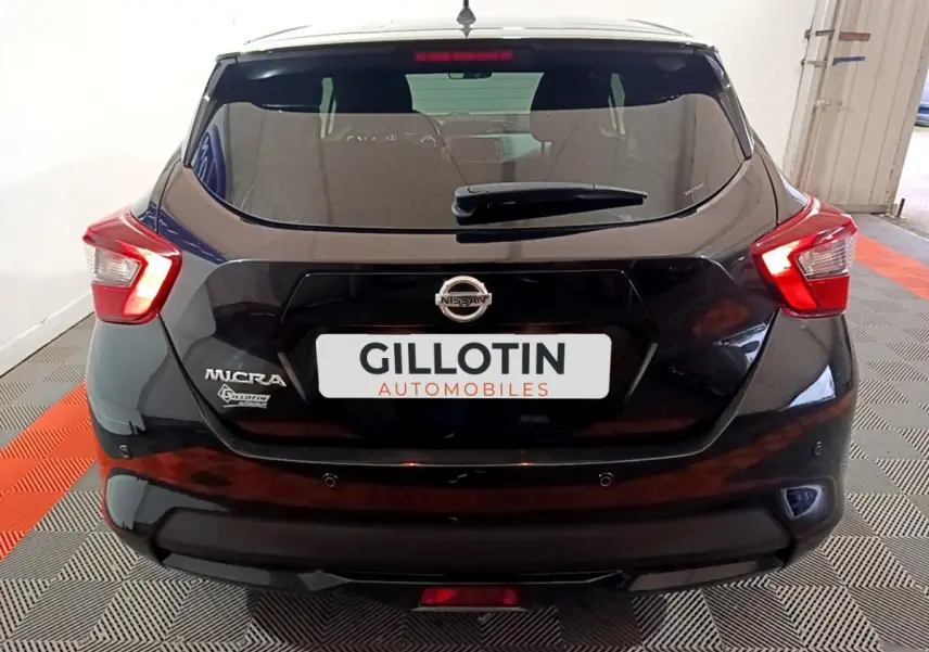 Vue arrière d'une Nissan Micra noire 2017 avec feux arrière allumés et logo visible sur un sol à damier rouge et gris.