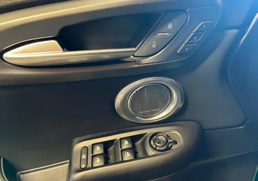 Détail de la porte côté conducteur de l'Alfa Romeo Tonale vert foncé, montrant les commandes de vitres et le haut-parleur rond.