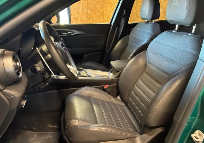 Vue intérieure côté conducteur de l'Alfa Romeo Tonale vert foncé, sièges en cuir noir avec logo Alfa Romeo brodé.