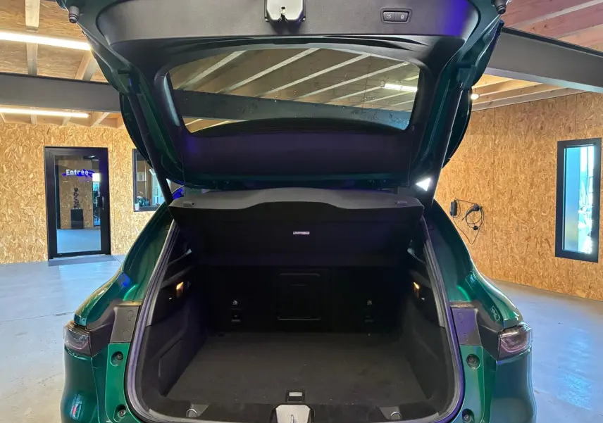 Coffre ouvert vu de l'arrière d'un Alfa Romeo Tonale vert foncé dans un garage avec intérieur noir visible.