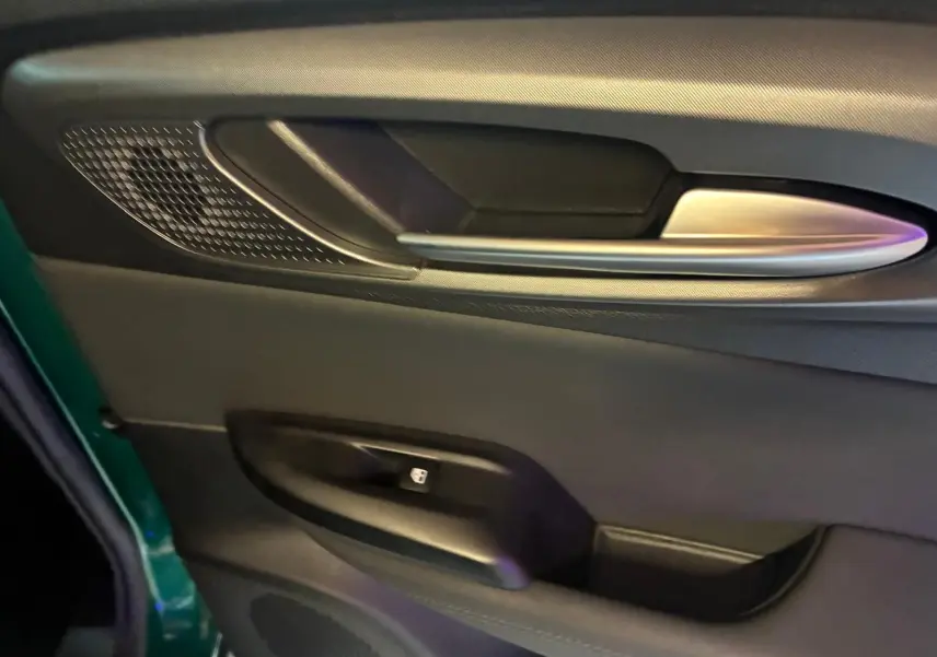 Gros plan sur la porte côté gauche d'une Alfa Romeo Tonale vert foncé, avec poignée argentée et commande de fenêtre.