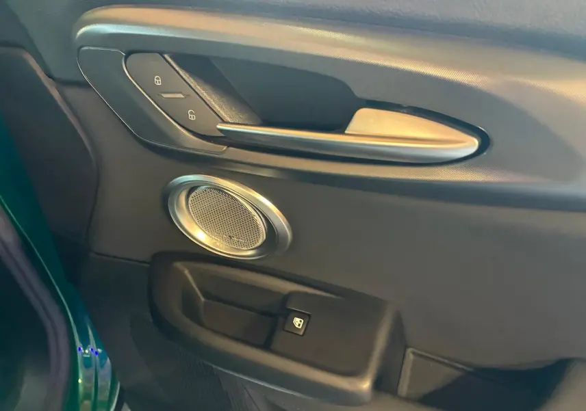 Détail de la porte côté gauche de l'Alfa Romeo Tonale vert foncé, avec poignée argentée et haut-parleur rond intégré.
