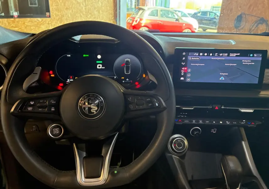 Vue intérieure centrée sur le volant noir d'Alfa Romeo Tonale 2022 avec tableau de bord digital et écran GPS lumineux.