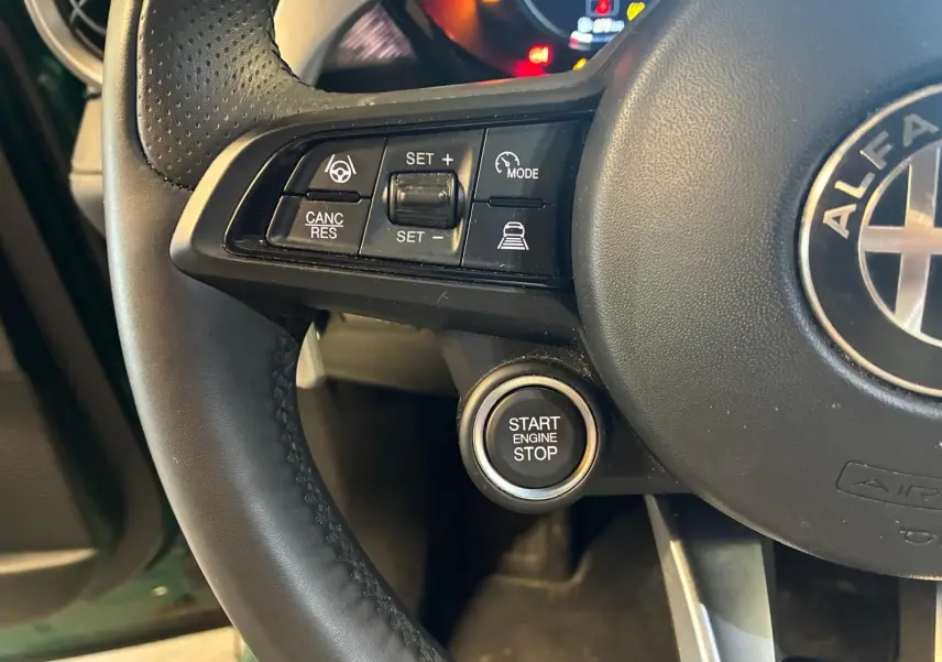 Gros plan sur le volant noir de l'Alfa Romeo Tonale avec boutons de régulateur et bouton start/stop visible.