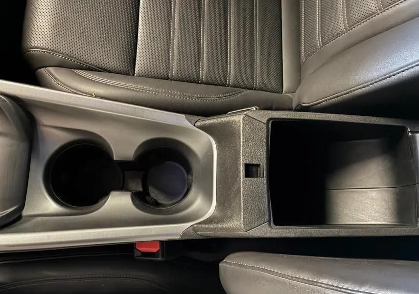 Vue en plongée sur la console centrale en cuir noir de l'Alfa Romeo Tonale 2022, avec porte-gobelets et rangement ouvert.