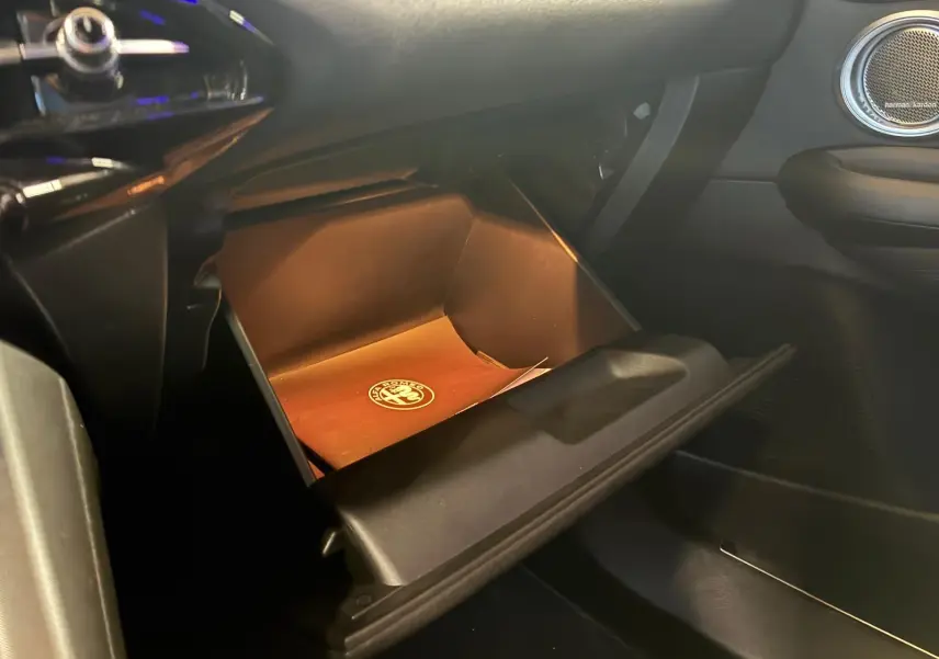 Intérieur de l'Alfa Romeo Tonale 2022, vue sur la boîte à gants ouverte côté passager avec manuel de bord visible.