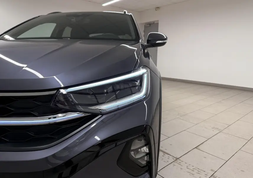 Gros plan sur l'avant droit du Volkswagen Taigo gris cendre, mettant en valeur le phare Matrix LED et la calandre noire.