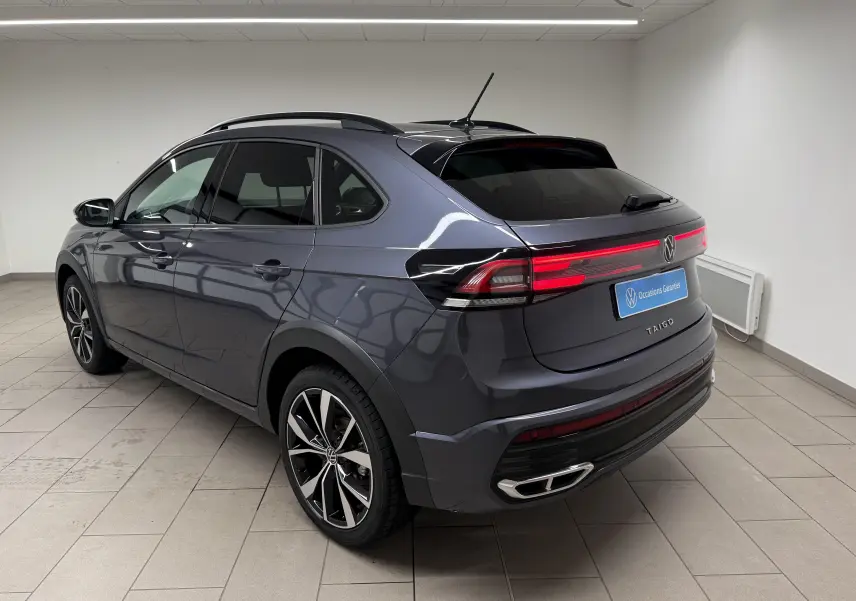 Vue 3/4 arrière droite du Volkswagen Taigo gris cendre avec jantes alliage noires et feux arrière LED allumés.