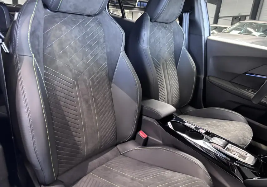 Vue intérieure rapprochée des sièges avant en Alcantara noir avec surpiqûres vertes et console centrale brillante.