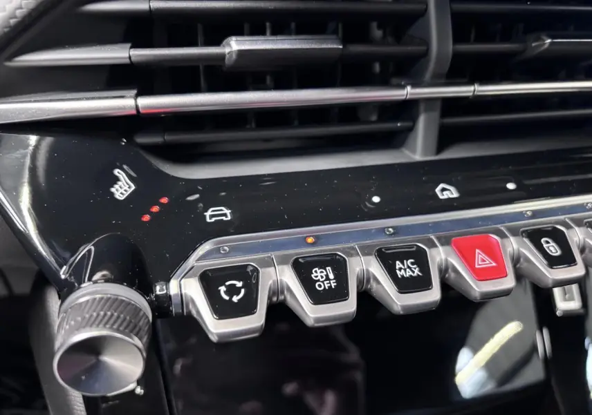 Gros plan sur la console centrale noire brillante du Peugeot 2008 1.2i Hybrid avec boutons de climatisation et siège chauffant.