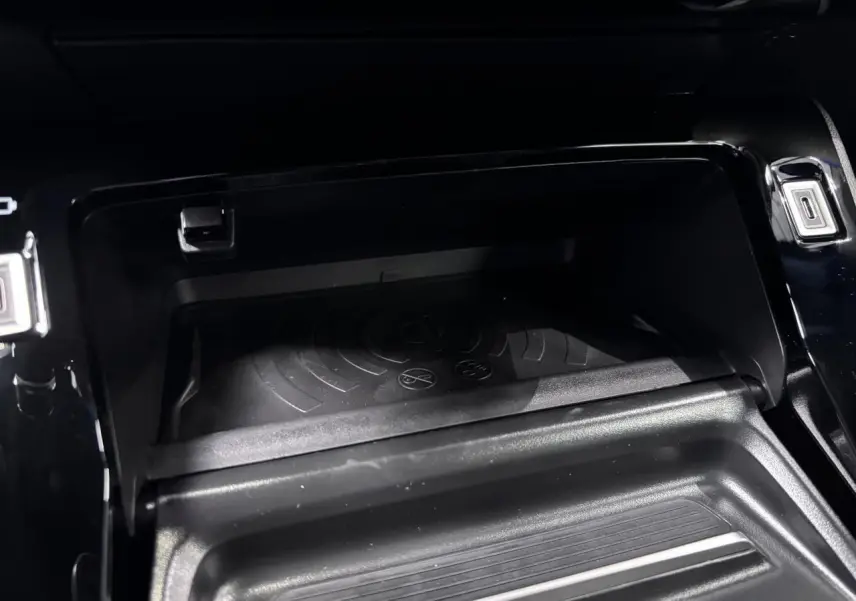 Vue rapprochée de la console centrale noire du Peugeot 2008 1.2i Hybrid avec chargeur smartphone sans fil intégré.