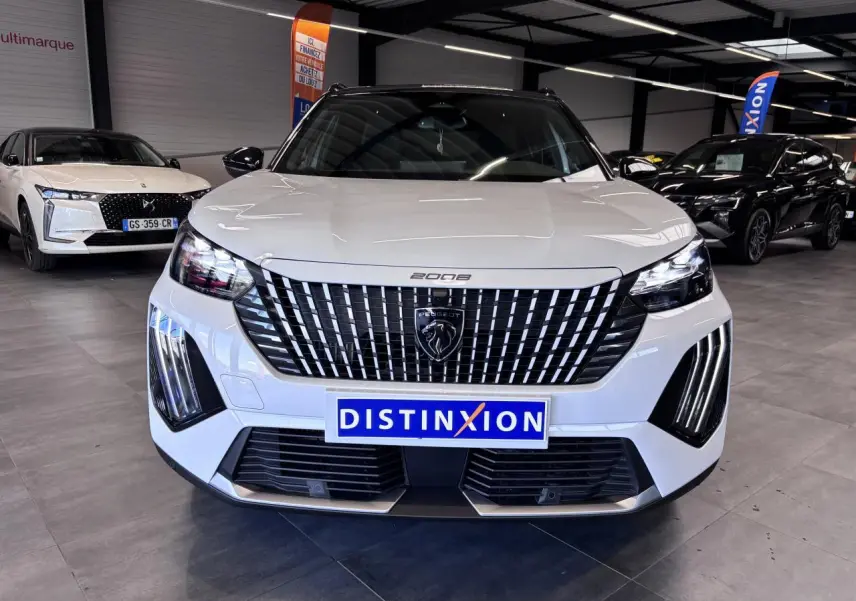 Vue frontale d'un Peugeot 2008 hybride blanc avec calandre verticale chromée et feux LED en griffes dans un showroom.