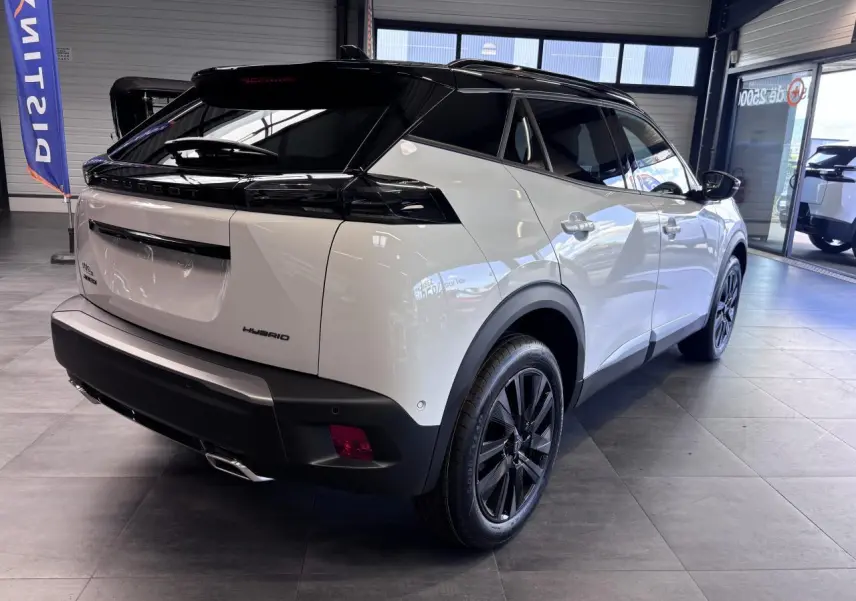 Vue 3/4 arrière droite du Peugeot 2008 hybride 2026 blanc avec toit noir et jantes alliage noires en showroom.