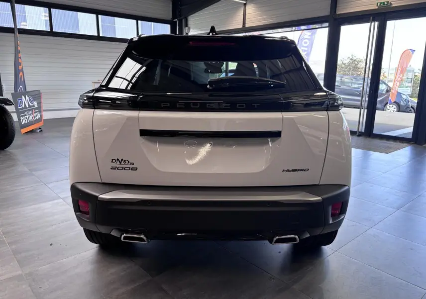 Vue arrière du Peugeot 2008 hybride blanc avec toit noir et double sortie d’échappement chromée en showroom.