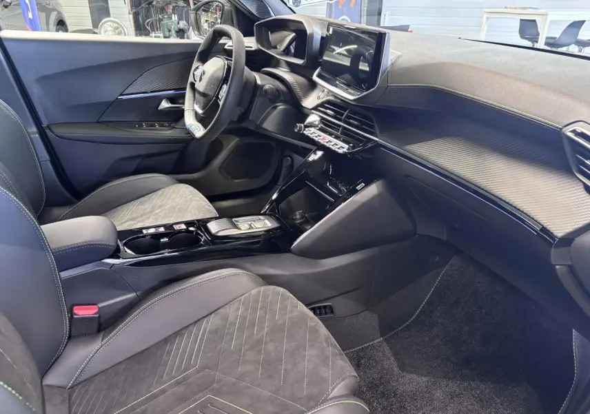 Intérieur avant droit du Peugeot 2008 1.2i Hybrid 2026 avec sellerie Alcantara noire et surpiqûres vertes, tableau de bord moderne.