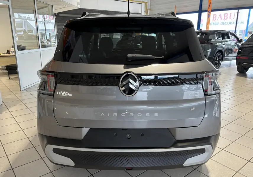 Vue arrière du Citroën C3 Aircross 2026 gris métallisé avec toit noir et feux arrière LED 3D en showroom.