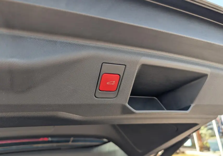 Bouton rouge d'ouverture électrique du hayon sur le panneau intérieur du coffre d'un Peugeot 5008 blanc.