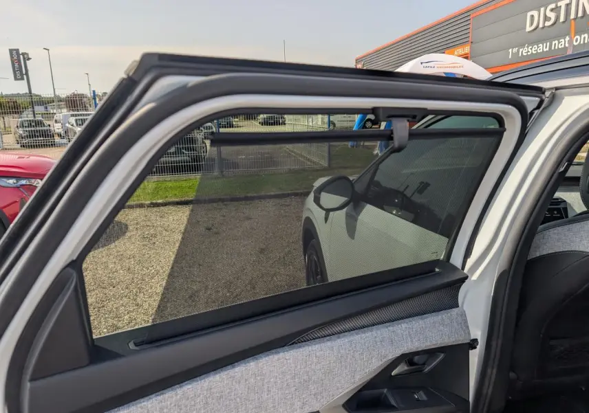 Vue intérieure sur la porte arrière gauche ouverte d’un Peugeot 5008 blanc, mettant en valeur le tissu gris et la protection pare-soleil.