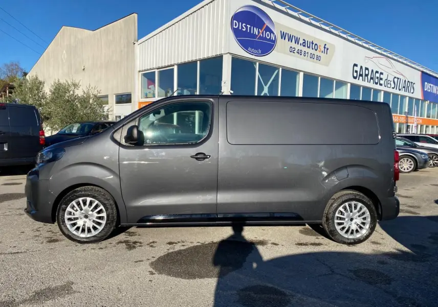 Peugeot Expert Fourgon gris titane vu de profil côté gauche, stationné devant un garage commercial.