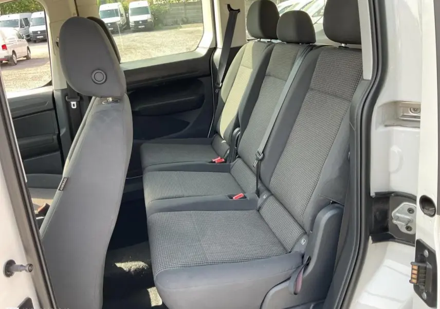 Vue intérieure côté droit sur les sièges arrière gris du Volkswagen Caddy blanc Candy avec porte coulissante ouverte.