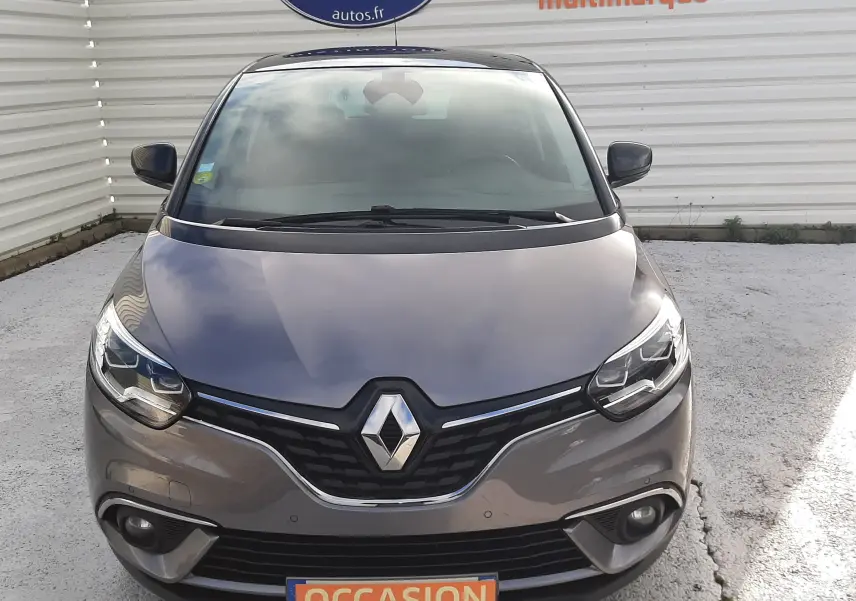 Vue avant d'une Renault Scénic IV gris Cassiopée avec toit noir, affichant une plaque "OCCASION" devant un mur blanc.