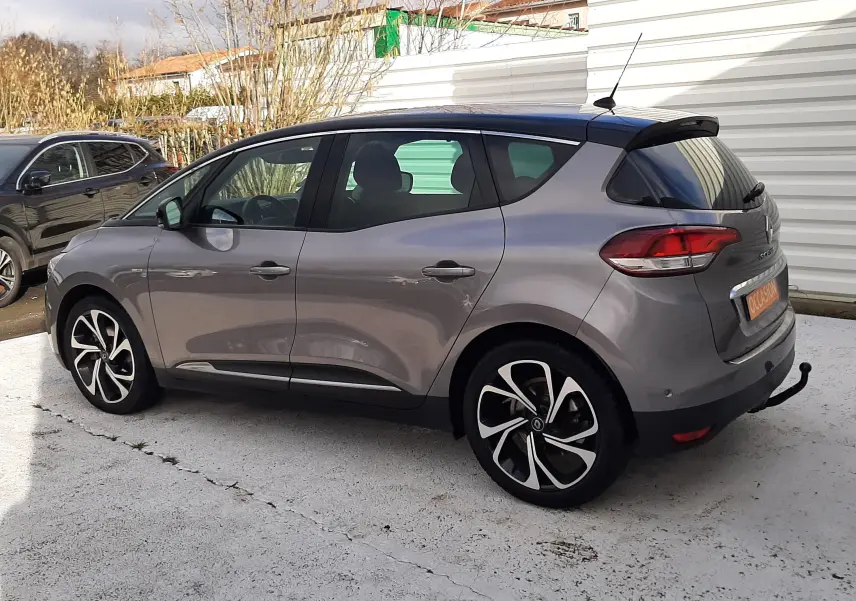 Gros plan sur la roue avant gauche du Renault Scénic IV gris Cassiopée avec jante alliage bicolore et logo Renault central.