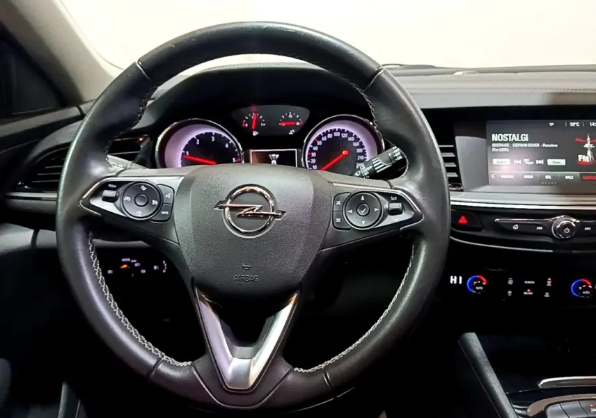 Vue intérieure centrée sur le volant cuir multifonctions et le tableau de bord avec écran tactile de l’Opel Insignia rouge.