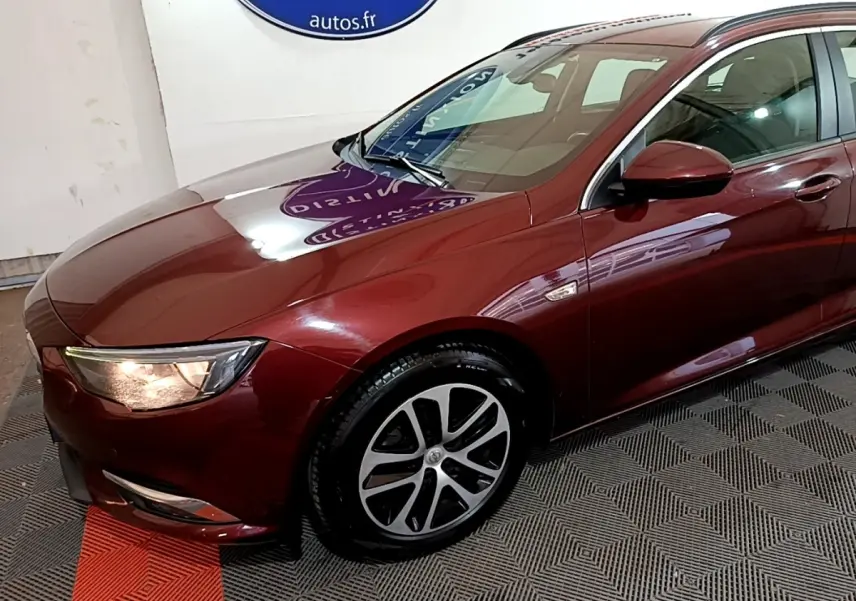 Vue 3/4 avant gauche d’une Opel Insignia rouge 2019 avec phares allumés et jantes alliage distinctives.