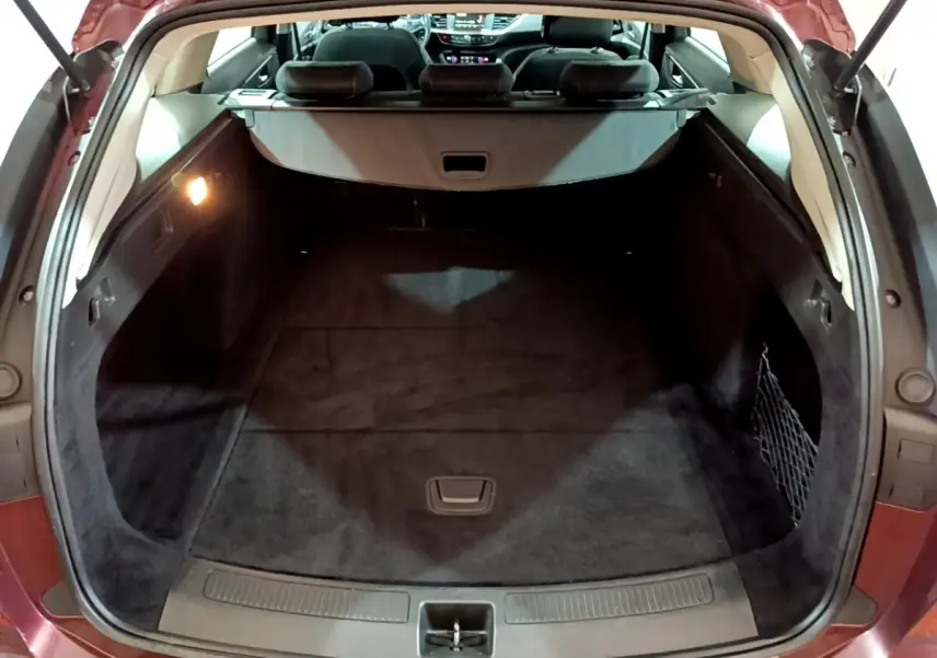 Coffre ouvert vu de l'arrière d'une Opel Insignia rouge, montrant un espace de chargement propre et bien éclairé.