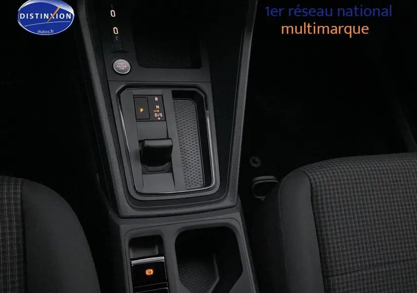 Vue rapprochée de la console centrale avec levier de vitesses automatique et sièges tissu noir à motifs du Volkswagen Caddy bleu métallisé.