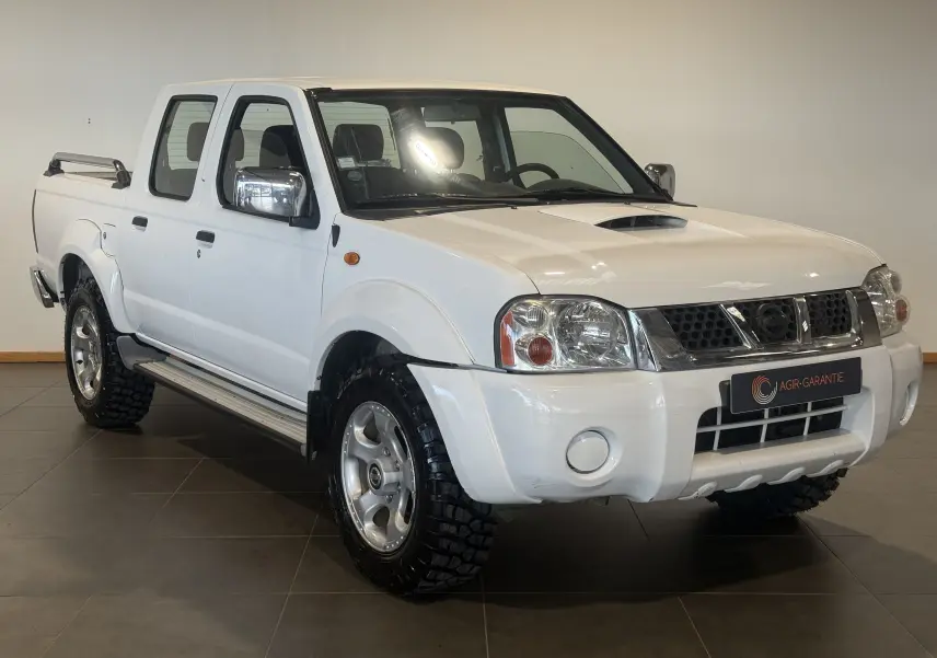 Vue 3/4 avant droite d’un Nissan Navara NP300 blanc de 2002, pickup double cabine avec pneus tout-terrain marqués.